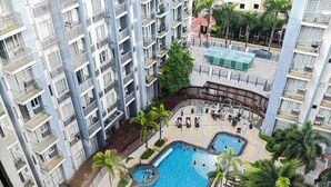 Un immeuble de grande hauteur doté de nombreux balcons, d’une piscine centrale et entouré de verdure.