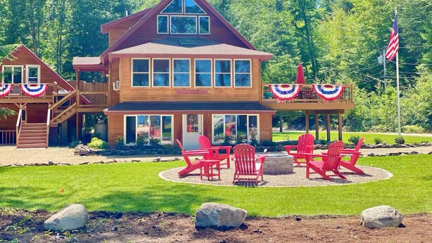 Una casa de madera de dos pisos con un porche cubierto y sillas Adirondack rojas.