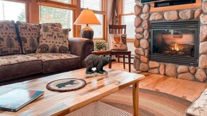 Un salón acogedor con chimenea de piedra, un sofá con cojines estampados de animales y una figurita de oso en la mesa de centro.