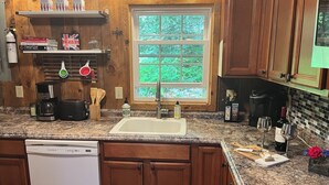 A kitchen with wooden cabinets, a granite countertop, a built-in dishwasher, a window with a view of greenery, and various kitchen appliances.