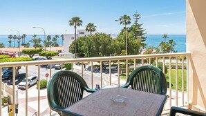 A balcony with two chairs and a table overlooking a street with cars and palm trees, and a view of the ocean. - Apartamentos Solset Nerja B (Nerja)