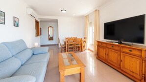 A living room with a sofa, a wooden coffee table, a TV on a wooden cabinet, and a dining area with chairs and a table. - Apartamentos Solset Nerja B (Nerja)