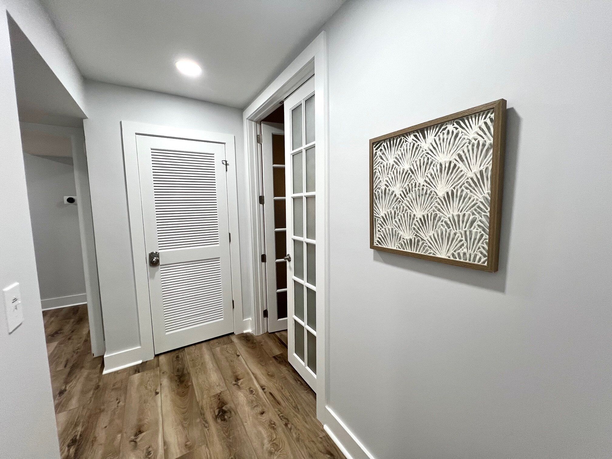 A hallway with a wooden floor, a white door with a window, and a wall-mounted decorative panel.