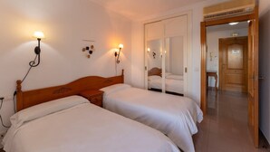 A hotel room with two single beds, a wooden headboard, bedside lamps, a mirror, and a door leading to another room. - Apartamentos Solset Nerja A (Nerja)