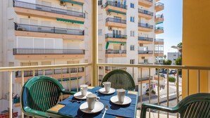 Ein Balkon mit zwei grünen Stühlen, einem Tisch gedeckt mit weißen Tassen und Untertassen und Blick auf mehrstöckige Häuser mit Balkonen.