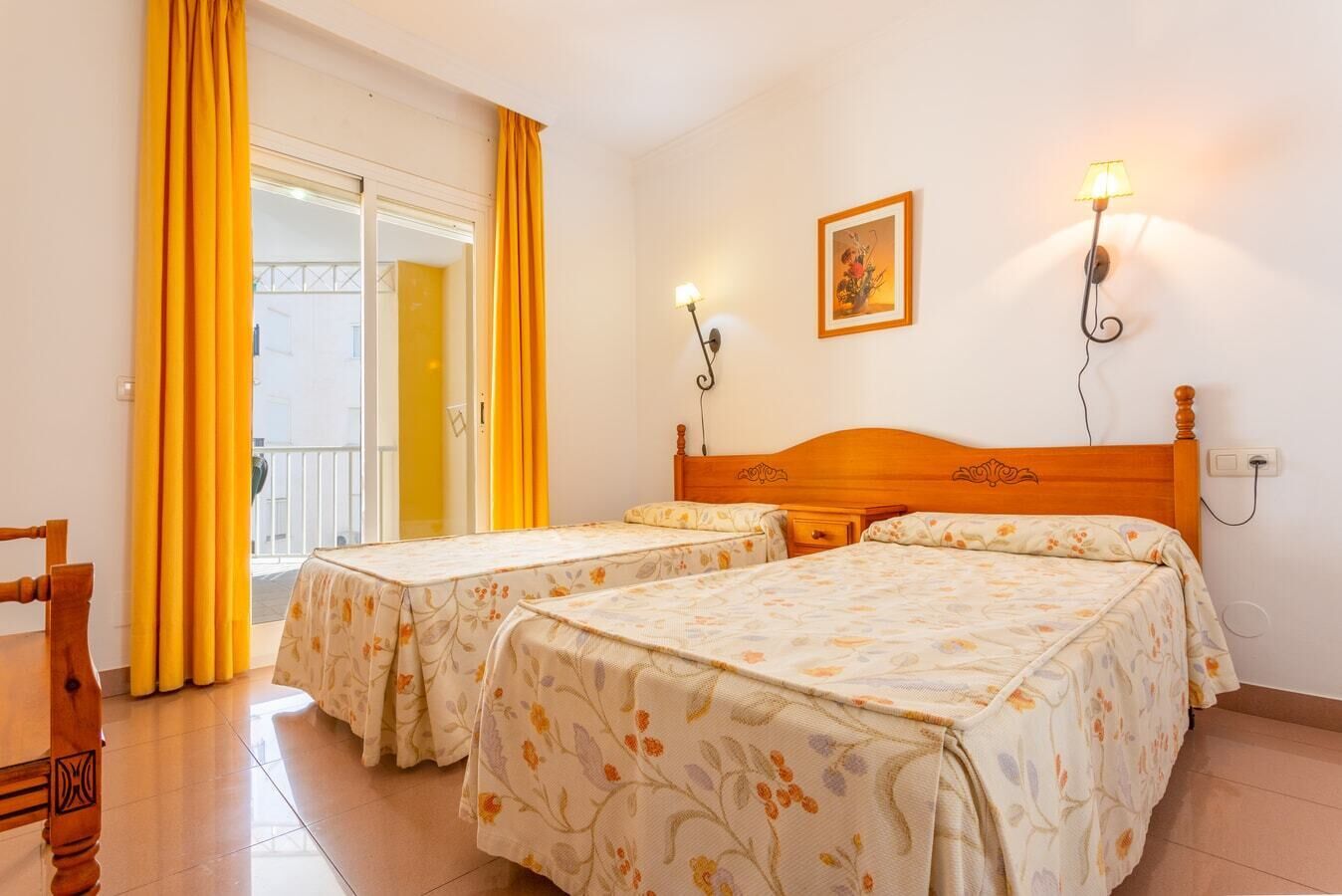 A hotel room with two beds, a wooden headboard, a painting on the wall, and a window with yellow curtains.