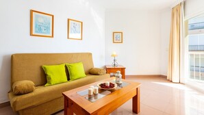 A living room with a sofa, a coffee table, and a lamp. There are framed pictures on the wall. - Apartamentos Solset Nerja C (Nerja)