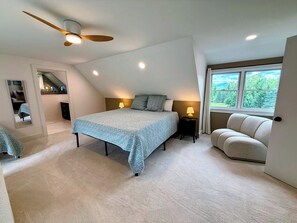 Une chambre à coucher avec un lit, des lampes de chevet, un ventilateur de plafond, une fenêtre donnant sur un beau paysage et un miroir.