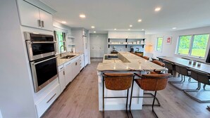 A modern kitchen with built-in appliances, a central island with bar stools, and a dining area with a long table. - 9FR Renovated home with beautiful views, large yard, dogs welcome! AC (Bethlehem)