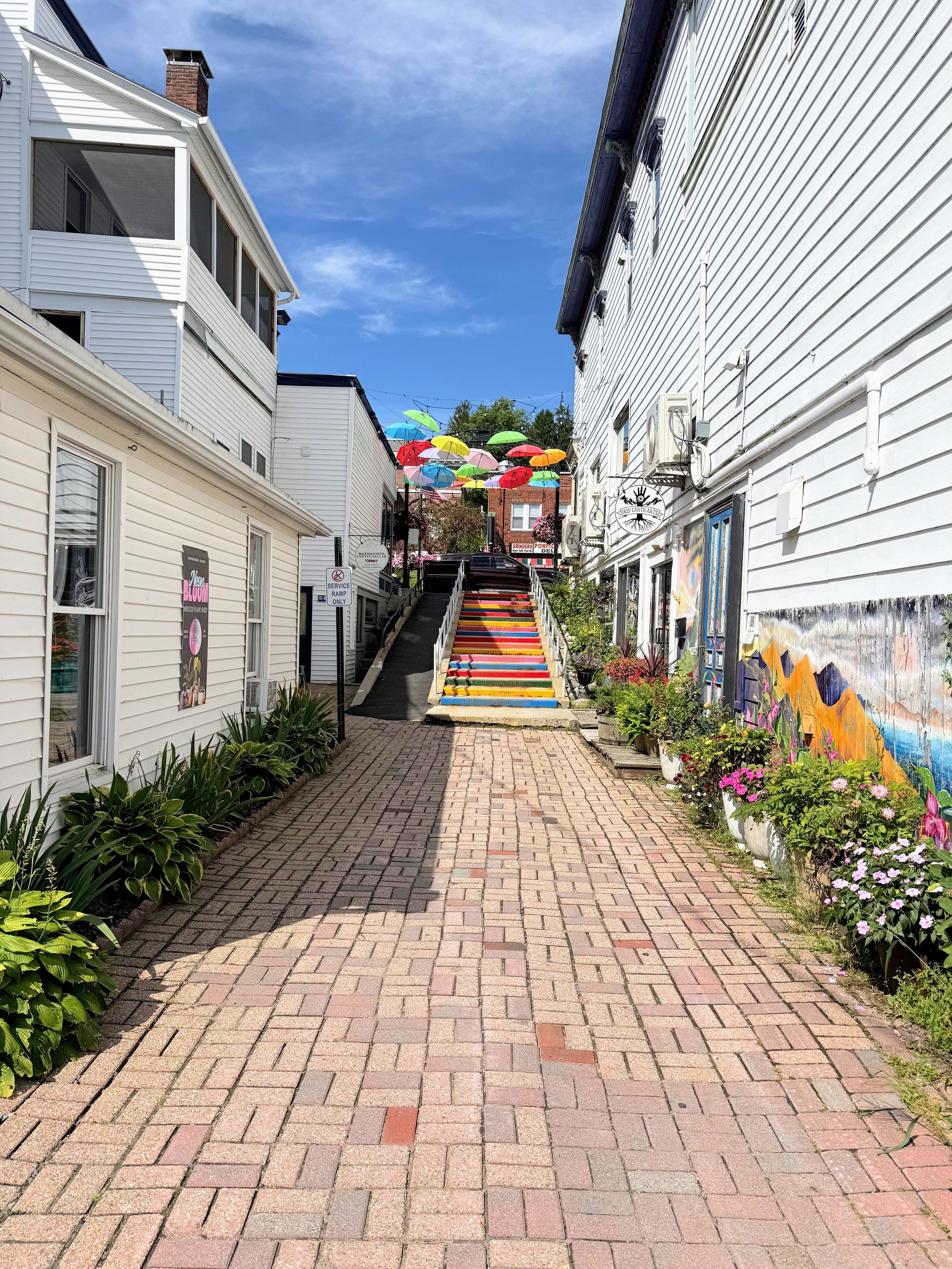 A narrow brick pathway leading to a building with colorful steps and a mural on the right wall.