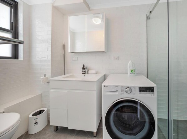 A modern bathroom with a white sink, mirror, toilet, and washing machine.