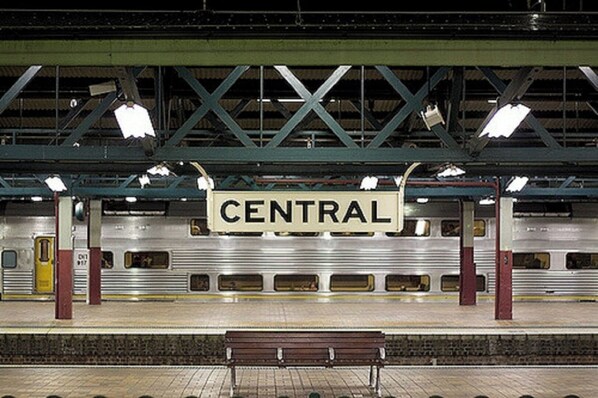 Un quai de gare avec un panneau indiquant « CENTRAL », un banc et un train.