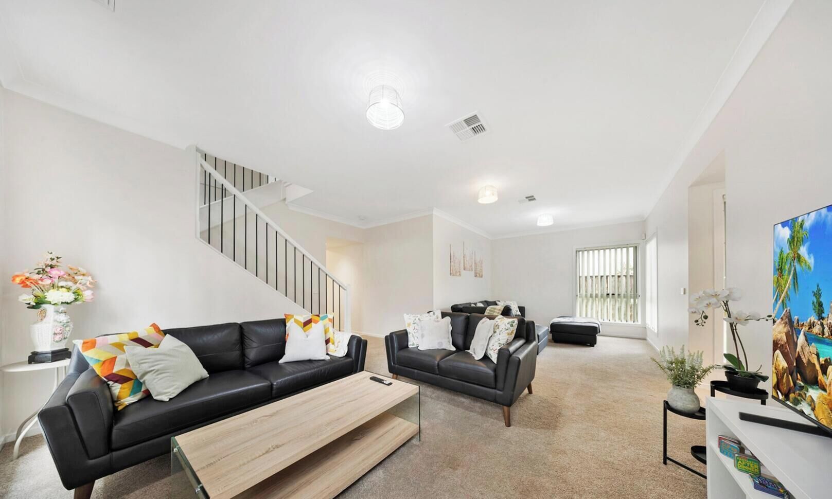 A modern living room with a staircase, two sofas, a coffee table, and a painting.