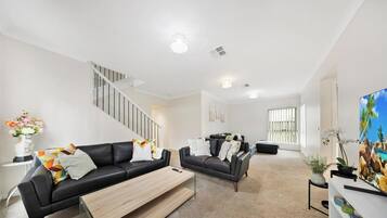 A modern living room with a staircase, two sofas, a coffee table, and a painting.
