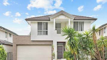 A two-story house with a garage, a balcony, and a small garden with palm trees.