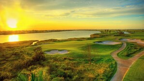 Ein Golfplatz mit einem Wasserhindernis, Sandbunkern und blauem Himmel.