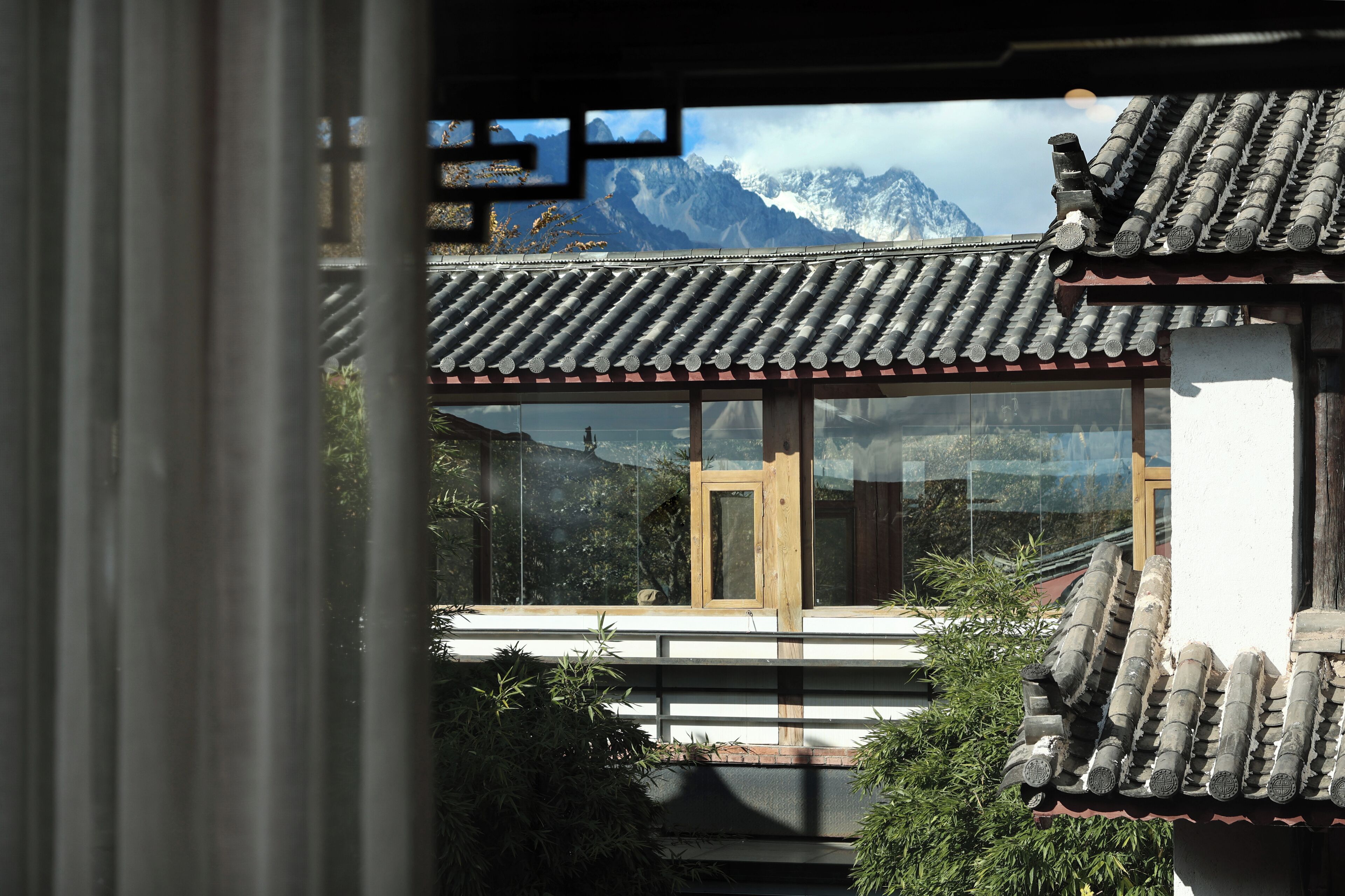A traditional building with a tiled roof and wooden door, surrounded by greenery and mountains in the background.