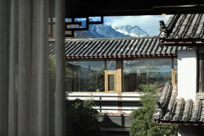 A traditional building with a tiled roof and wooden door, surrounded by greenery and mountains in the background. - Yulong Sadhu Inn (Lijiang)