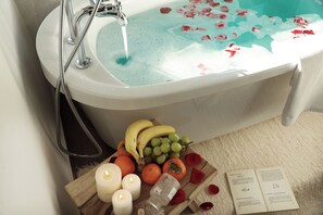 A bathtub with rose petals, a fruit basket, candles, and a booklet. - Yulong Sadhu Inn (Lijiang)