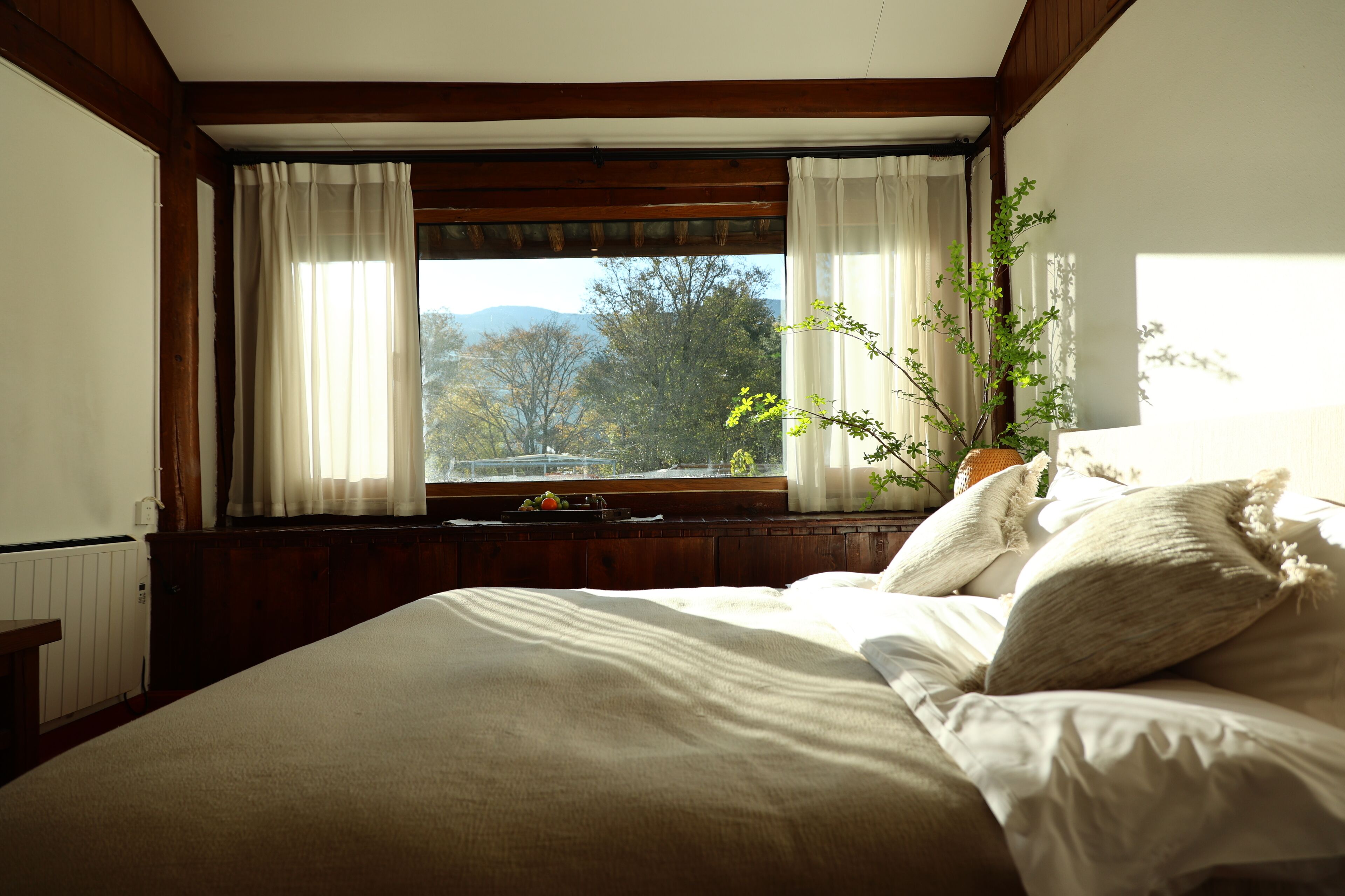 A bedroom with a large bed, wooden headboard, and a window with curtains.