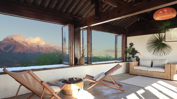 A sunlit room with a view of mountains, a wicker sofa, and two lounge chairs. - Yulong Sadhu Inn (Lijiang)
