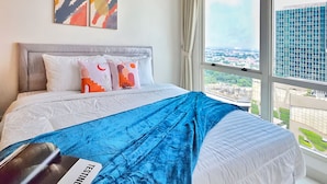 A modern hotel room with a large bed, a view of the city, and abstract art on the wall. - Kenzi By SanLiving - 2BR - Kelapa Gading (Jakarta)