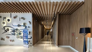 A modern hotel corridor with wooden paneling, a polished floor, and decorative wall art. - Kenzi By SanLiving - 2BR - Kelapa Gading (Jakarta)