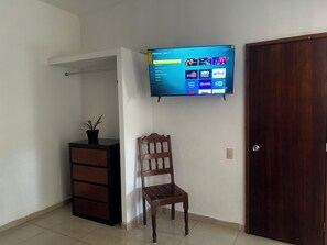 A room with a TV mounted on the wall, a wooden chair, a small cabinet, and a door.