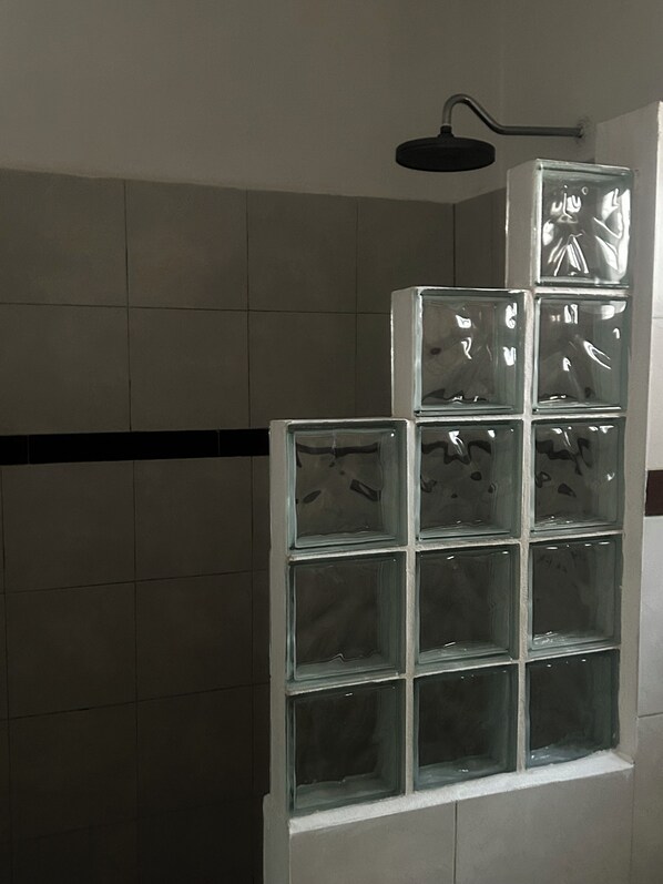 A bathroom with a tiled wall, a shower area, and a glass block shelf unit.