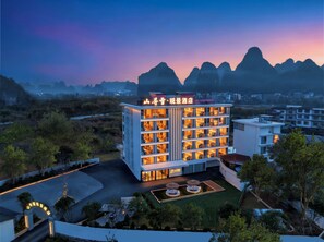 A hotel with multiple floors, a well-lit entrance, and a view of distant mountains.