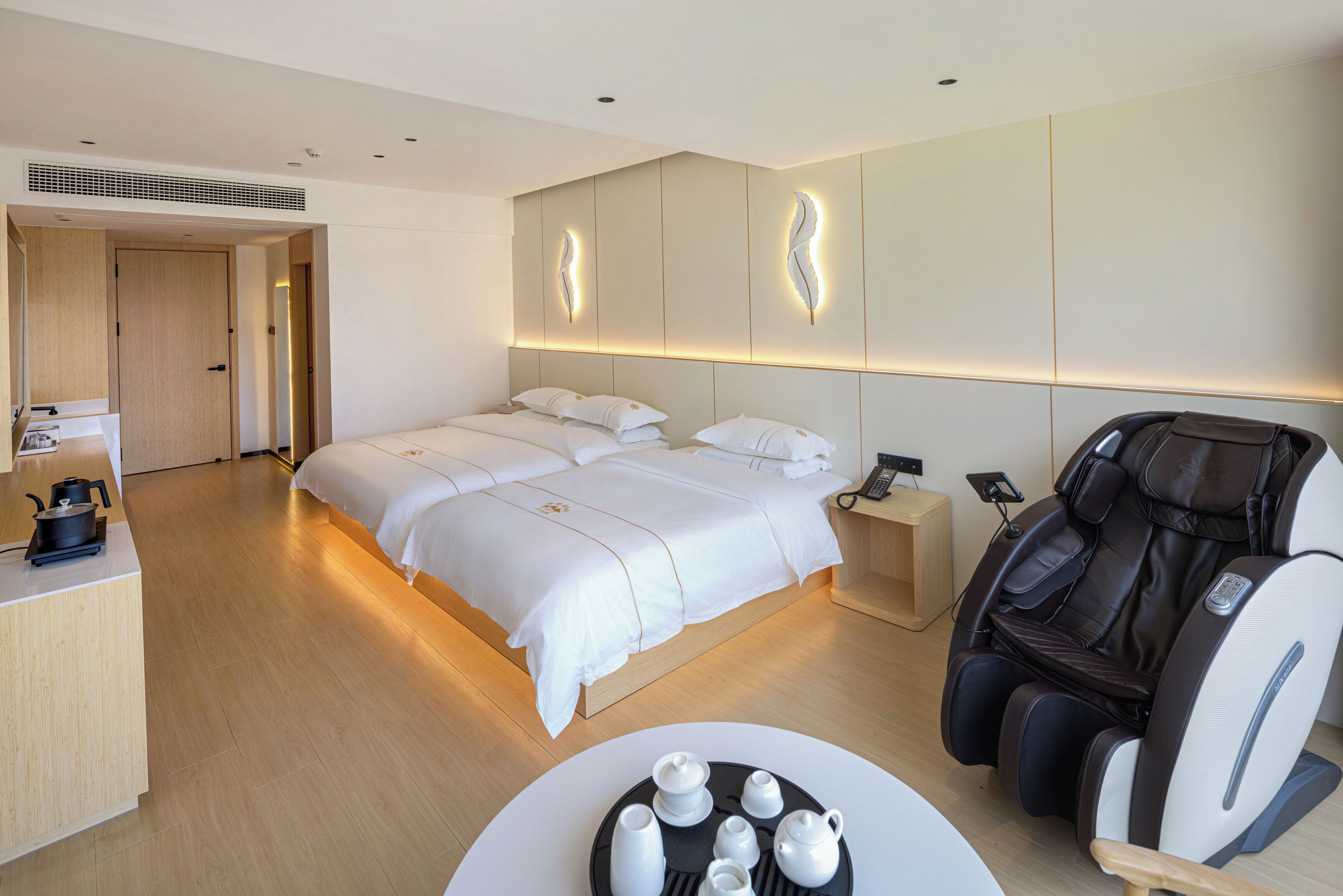 Une chambre d’hôtel moderne dotée d’un grand lit, d’un fauteuil massant, d’une petite table avec un service à thé et d’un bureau en bois.