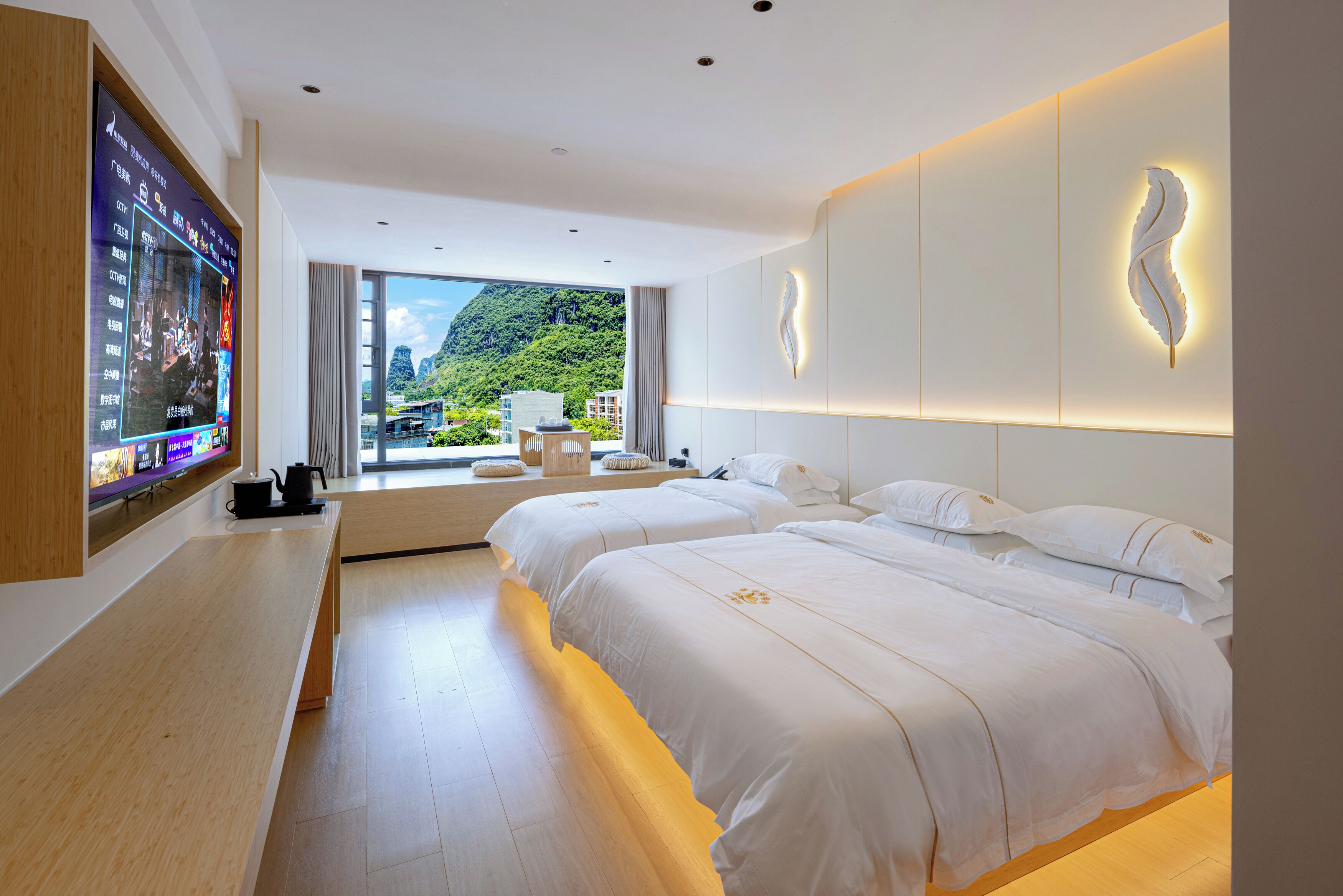 Habitación de hotel moderna con televisor grande, dos camas, un banco de madera y vistas a la montaña.