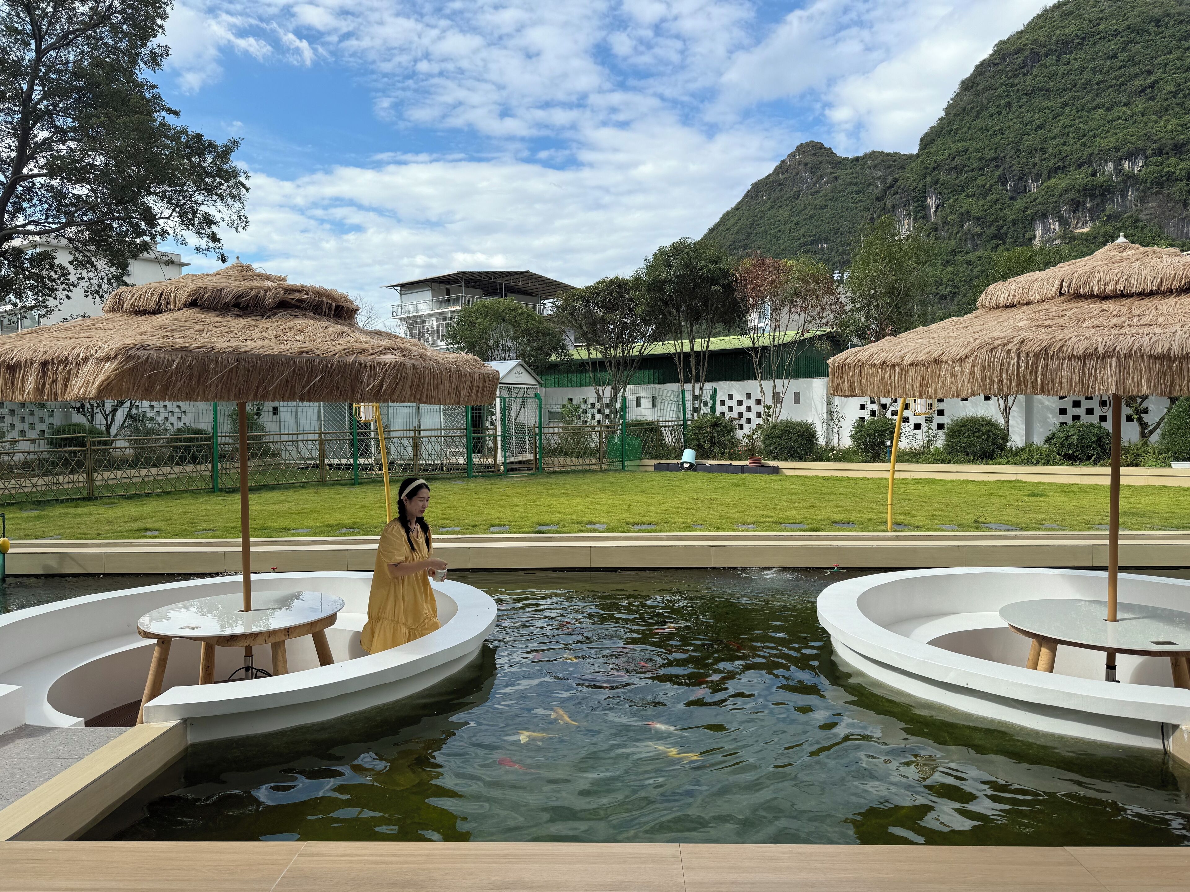 A serene outdoor pool area with thatched umbrellas and a person standing by the water.