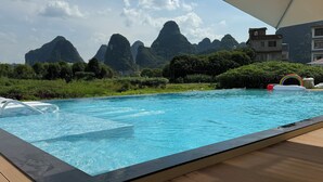 A swimming pool with clear blue water, surrounded by lush greenery and mountains in the background. - Mountain Search Snow View Hotel (Guilin)