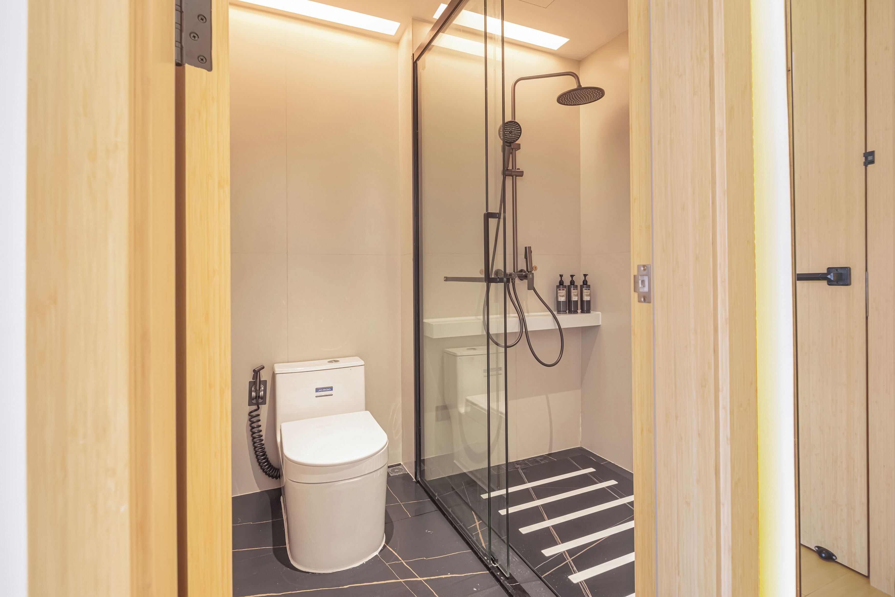 A modern bathroom with a glass-enclosed shower, a white toilet, and a tiled floor.