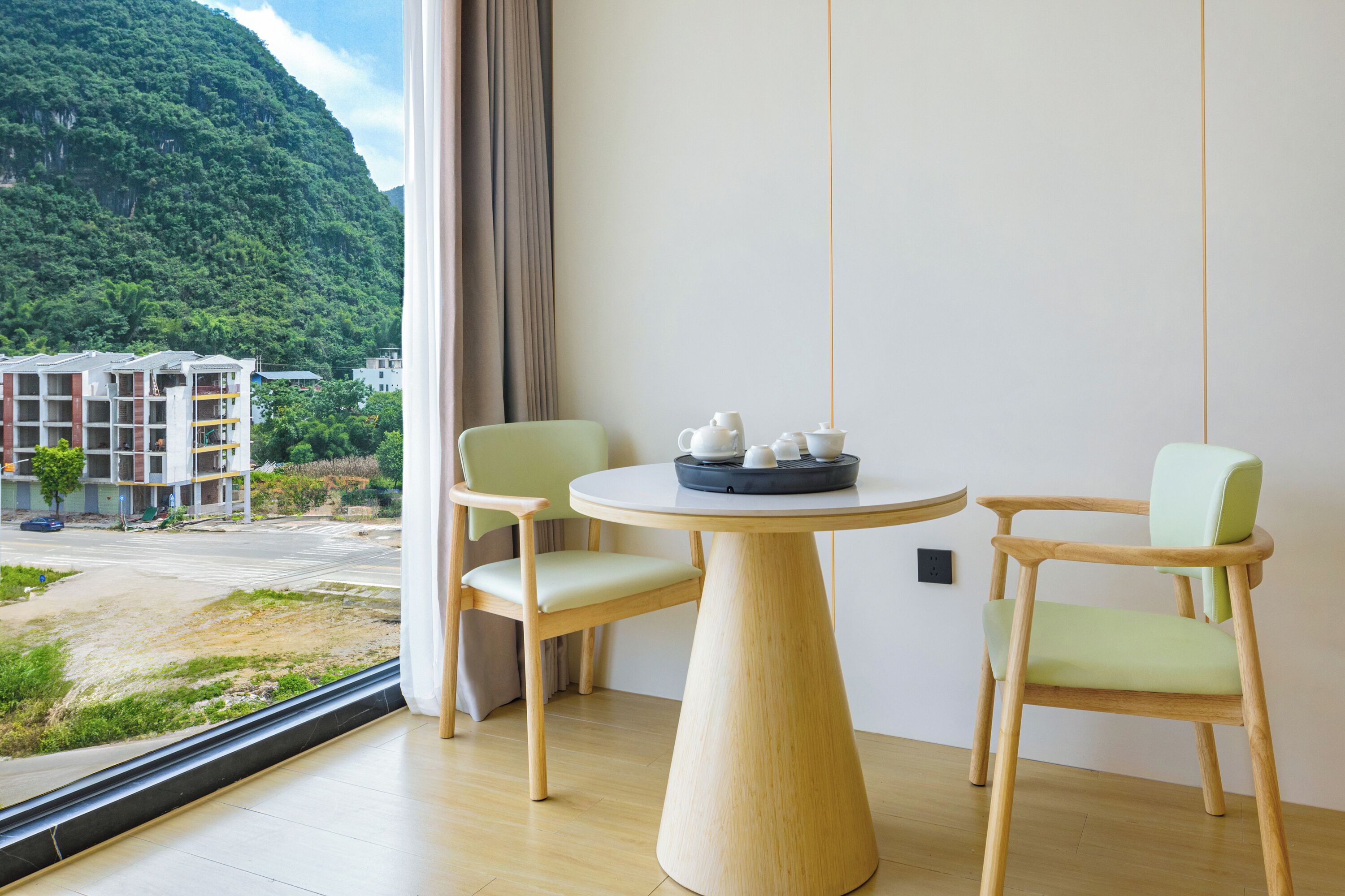 A room with a round wooden table, two chairs, and a view of a mountainous landscape through a window.