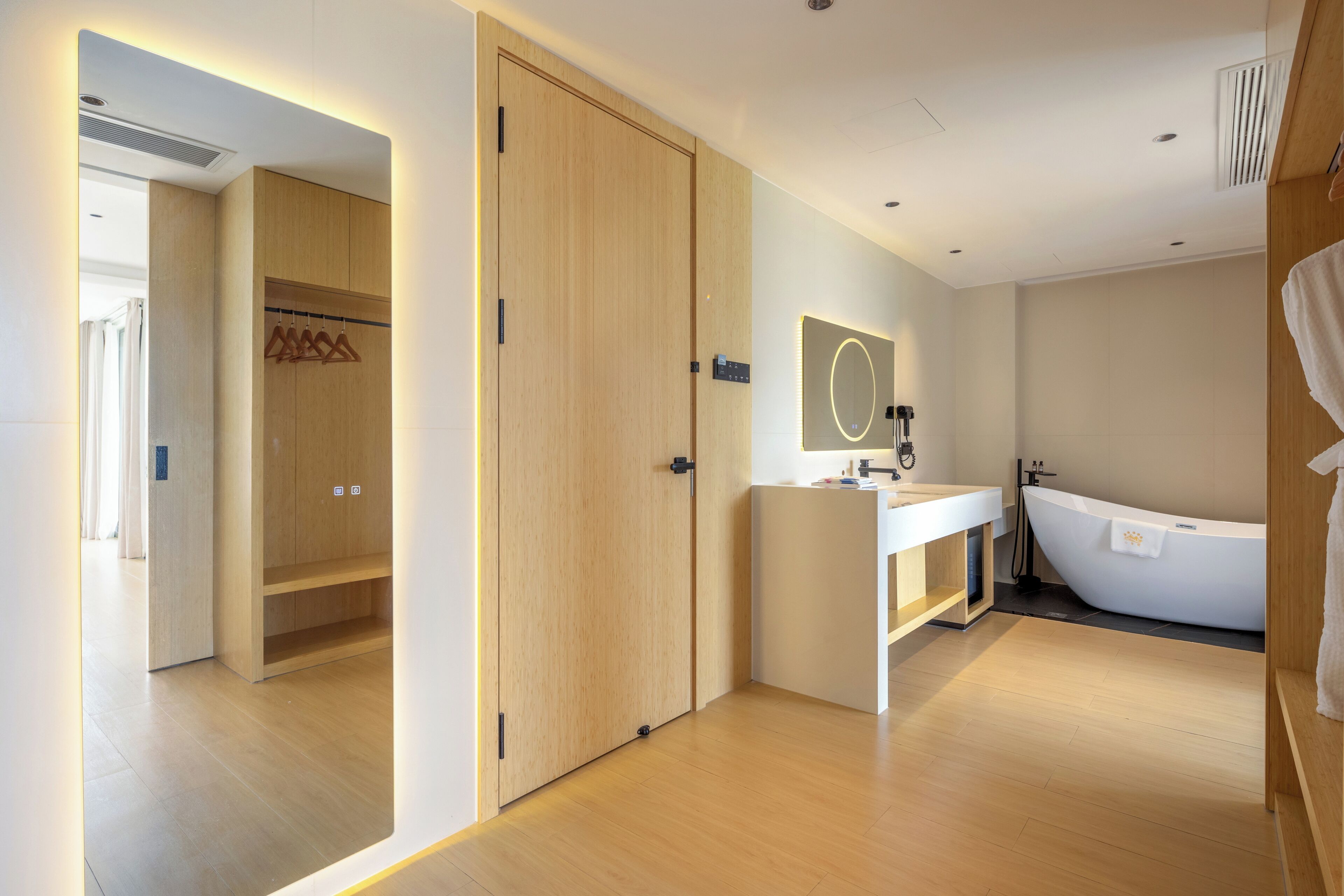 A modern bathroom with a freestanding bathtub, a mirror with a light halo, and wooden flooring.