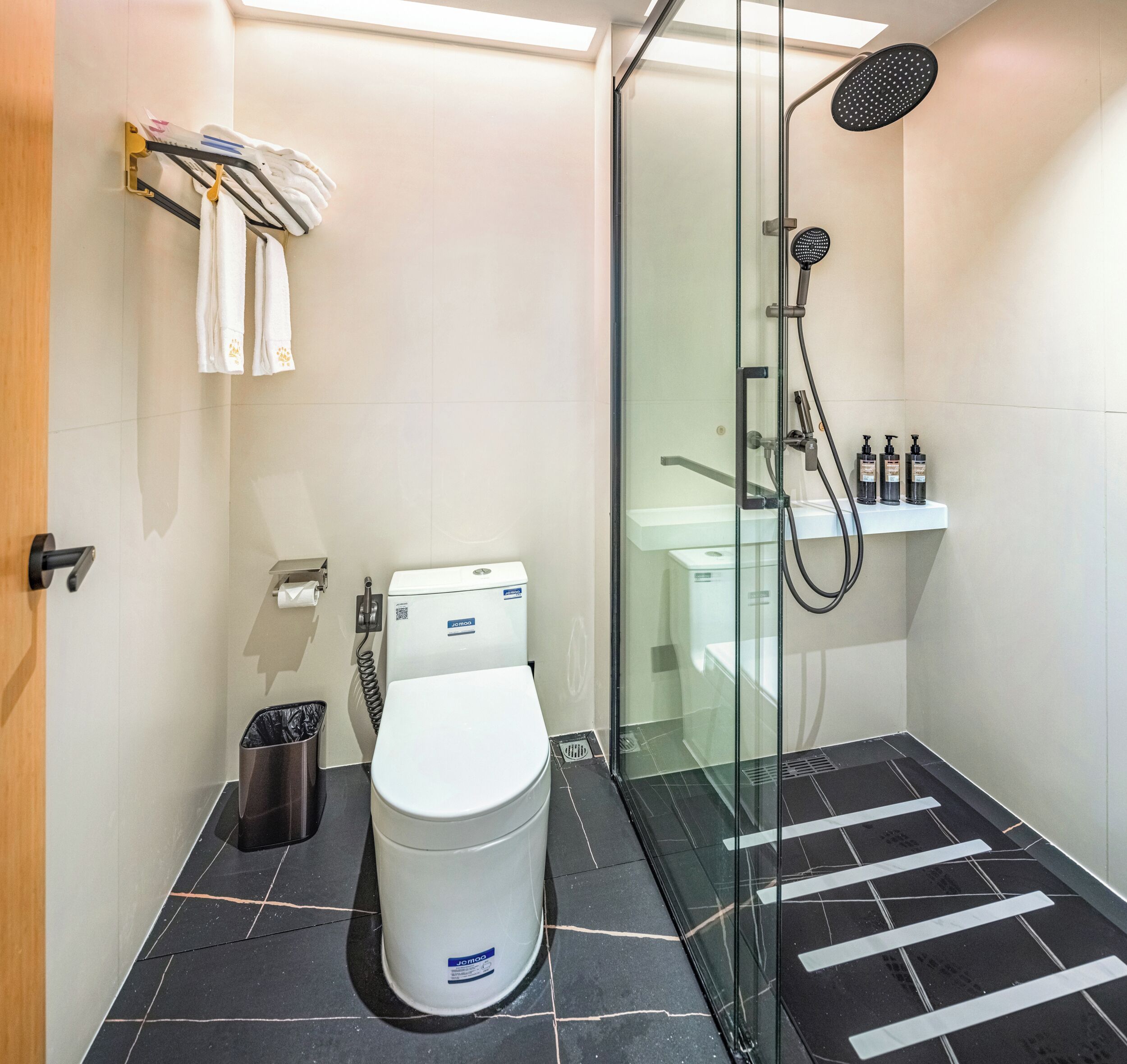 A modern bathroom with a toilet, glass shower enclosure, and a sink with toiletries.