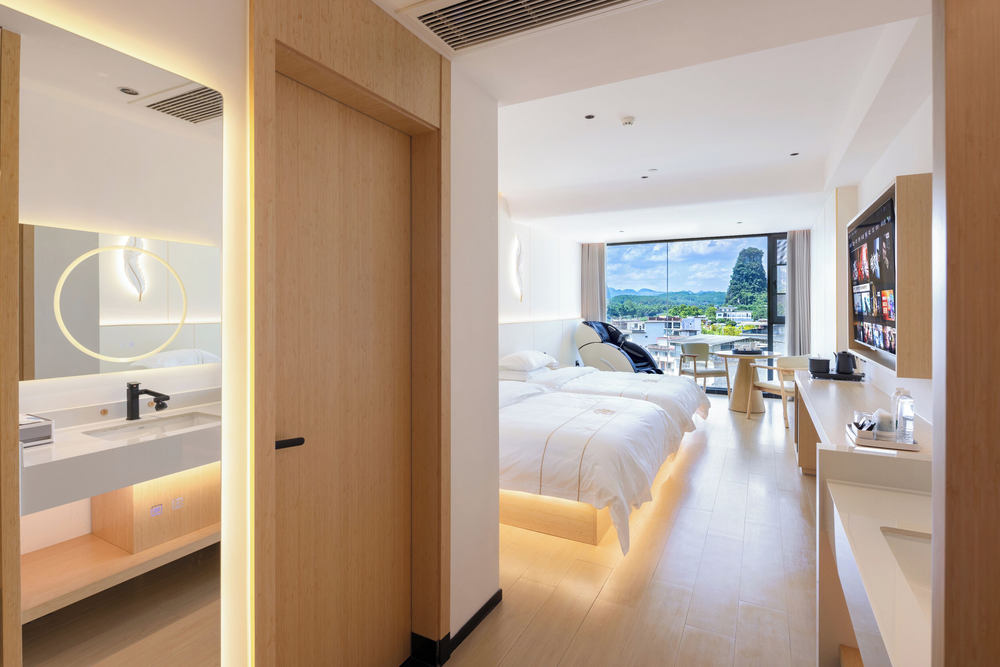 A modern hotel room with a large bed, a desk, a bathroom with a sink and mirror, and a view of the city.