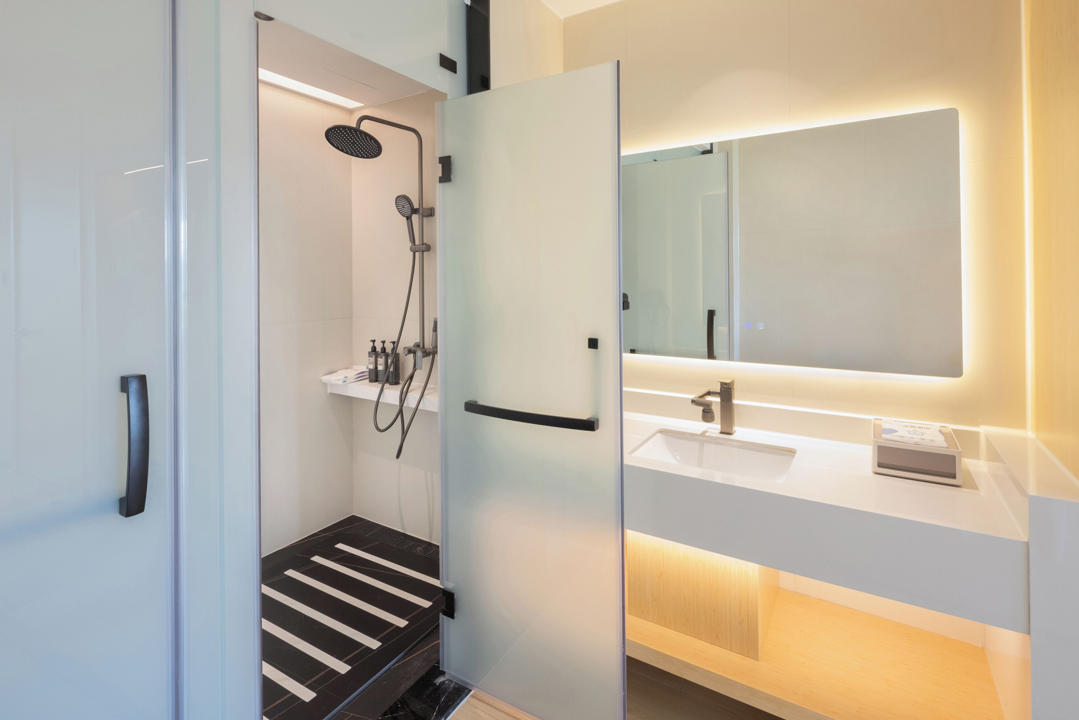 Un baño moderno con cabina de ducha de vidrio, un lavabo blanco y un espejo grande.