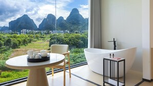 A modern hotel room with a large window offering a view of green hills and mountains. - Mountain Search Snow View Hotel (Guilin)