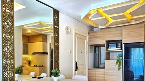 A modern kitchen with a dining area, featuring a wooden table and chairs, a microwave, and a refrigerator. - Amethyst By SanLiving - 3BR & 1 Maid Room - Central Park Mall (Jakarta)