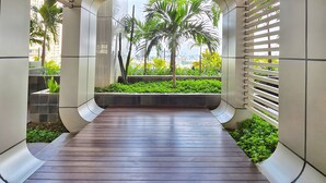 A corridor with a wooden floor, white walls, and a view of palm trees and greenery. - Amethyst By SanLiving - 3BR & 1 Maid Room - Central Park Mall (Jakarta)