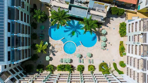Ein Luftbild eines Hotels mit einem zentral gelegenen Schwimmbad, umgeben von Palmen und Liegestühlen.