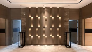 Un vestíbulo moderno con piso de mármol, una pared con paneles de luz verticales y dos columnas negras.