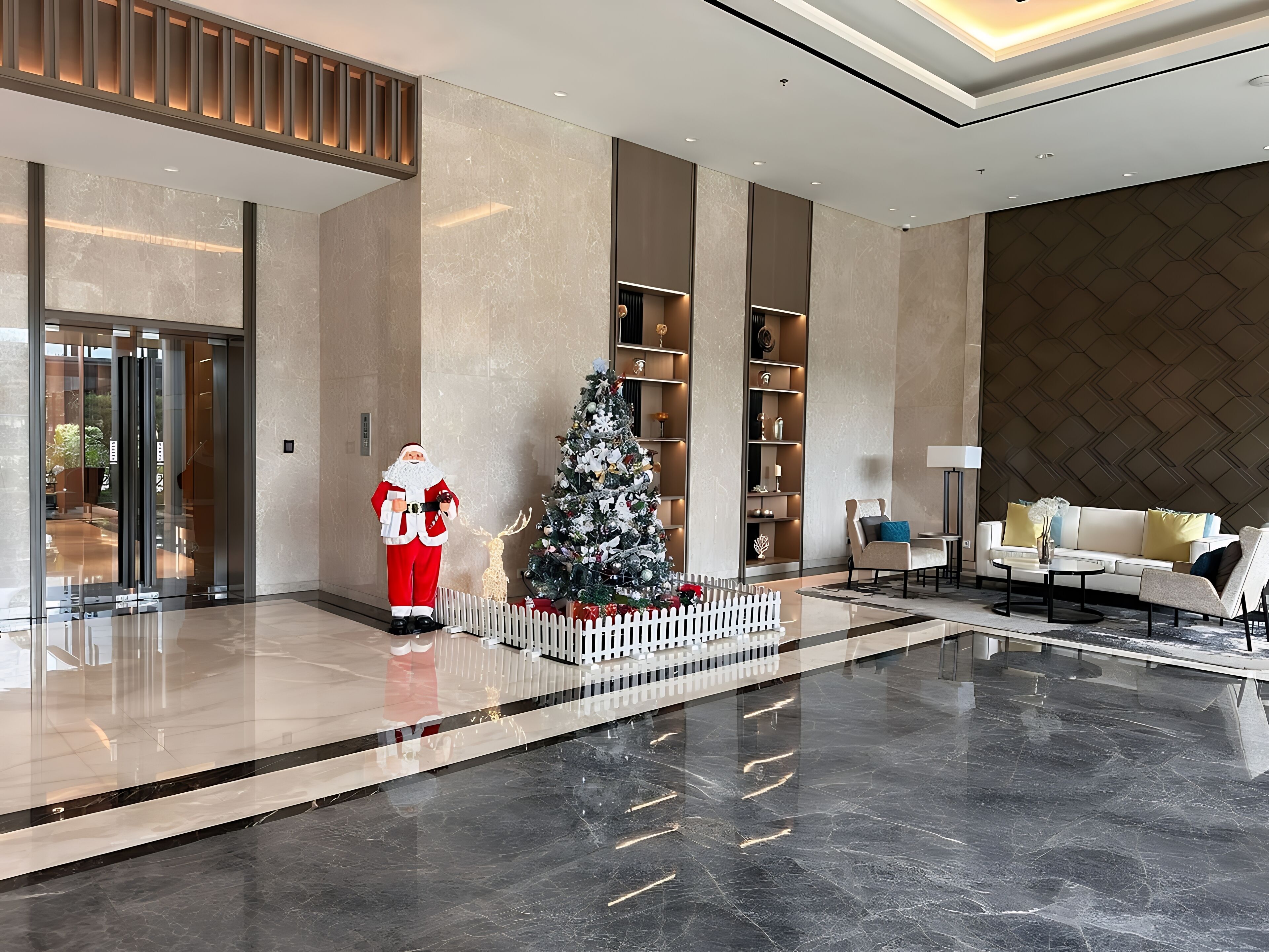 A modern lobby with a Christmas tree, a Santa Claus figure, and a white picket fence.