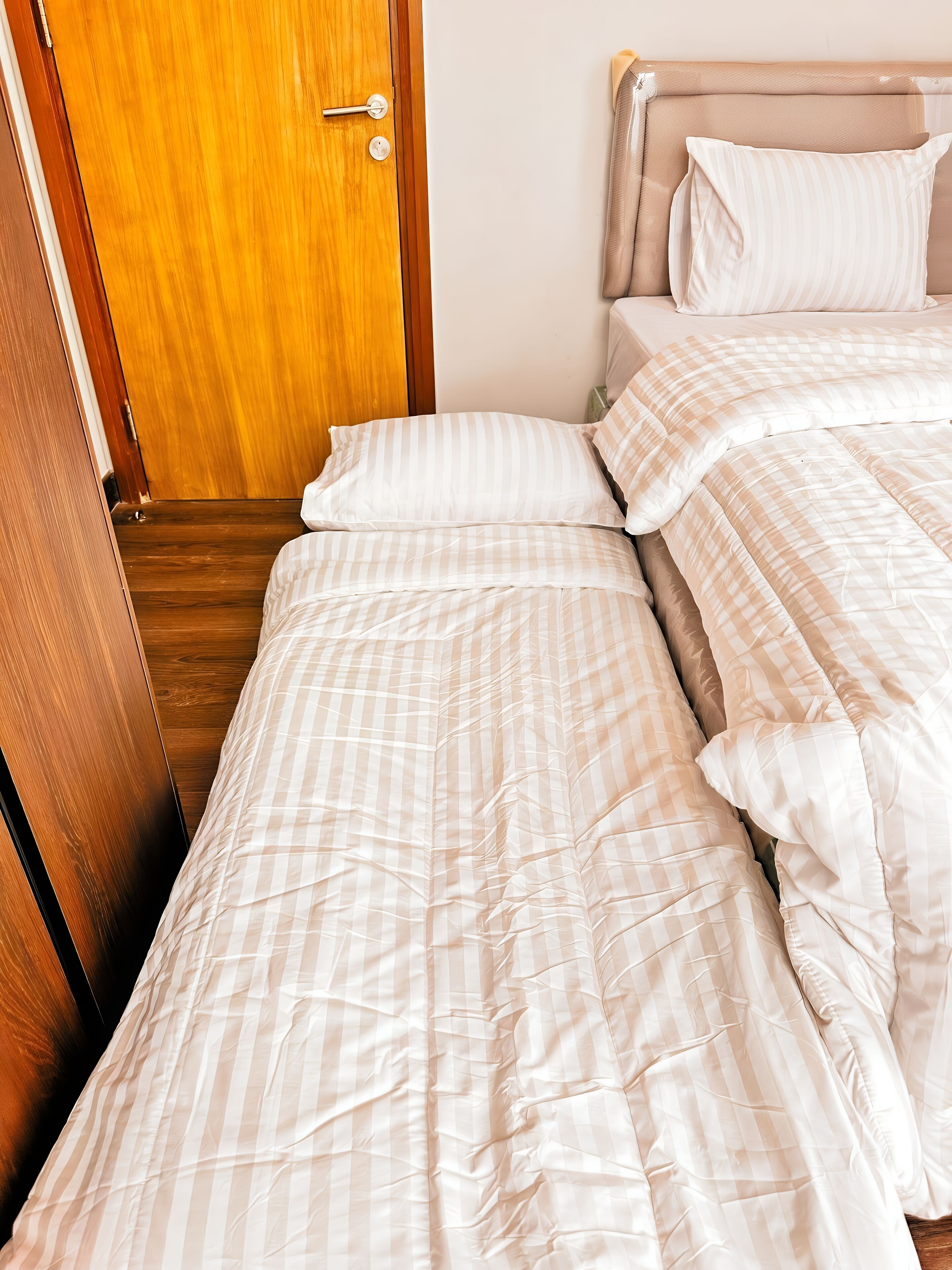 A neatly made bed with striped bedding, a wooden door, and a headboard.