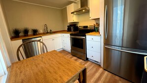 Een keuken met witte kastjes, een roestvrijstalen koelkast, een houten tafel en een stoel.