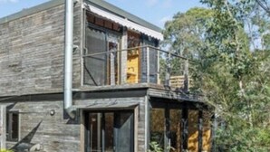 A rustic wooden house with a balcony, large windows, and a chimney.