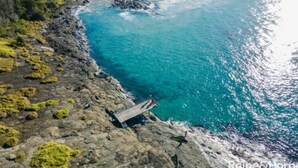 A coastal location with a rocky shoreline, clear blue waters, and a wooden pier.